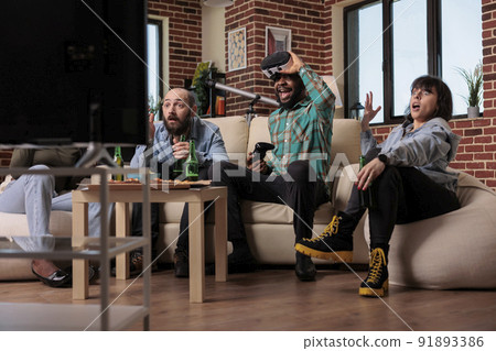 Cheerful friends feeling happy about winning video games, celebrating win and victory together with bottles of beer and pizza at home. Young people enjoying leisure time with gaming and alcohol. Cheerful friends feeling happy about winning video games, celebrating win and victory together with bottles of beer and pizza at home. Young people enjoying leisure time with gaming and alcohol. 91893386