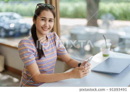Self Employed, Business Owner, Portrait of an Asian woman using a smartphone mobile and computer working online or shopping online through the Internet at home. 91893491
