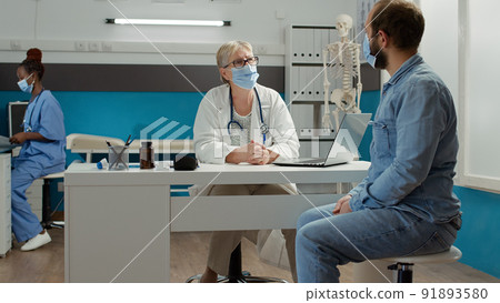 Physician and male patient having conversation at medical examination in cabinet. Doing health care consultation at checkup appointment to give support and prescription medicine during pandemic. 91893580