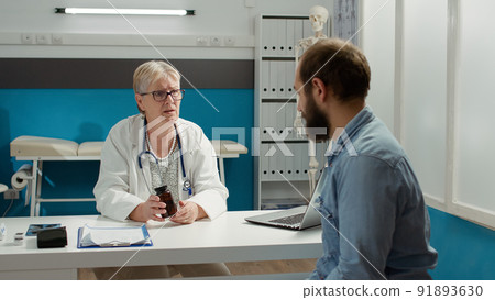 General practitioner giving bottle of pills to cure man with sickness at checkup visit in medical cabinet. Explaining prescription treatment in flask with medication at consultation appointment. 91893630