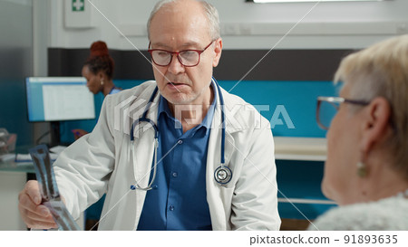 Medic and old patient analyzing bones radiography at checkup visit appointment for recovery. Health specialist showing x ray diagnosis and scan results to treat sickness with medicine. Medic and old patient analyzing bones radiography at checkup visit appointment for recovery. Health specialist showing x ray diagnosis and scan results to treat sickness with medicine. 91893635