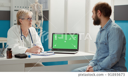 Senior doctor and patient looking at laptop with greenscreen at checkup visit. Man and woman using isolated template with blank chromakey background and mockup copyspace on display. Senior doctor and patient looking at laptop with greenscreen at checkup visit. Man and woman using isolated template with blank chromakey background and mockup copyspace on display. 91893673