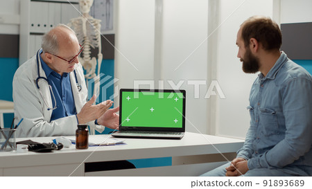 General practitioner pointing at laptop display with greenscreen, meeting at checkup visit. Looking at blank copyspace background with isolated mockup and chroma key template. Tripod shot. General practitioner pointing at laptop display with greenscreen, meeting at checkup visit. Looking at blank copyspace background with isolated mockup and chroma key template. Tripod shot. 91893689