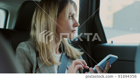 Beautiful woman typing on her smartphone in the car. Lady manager looking at phone in the back seat of a car. 91894356
