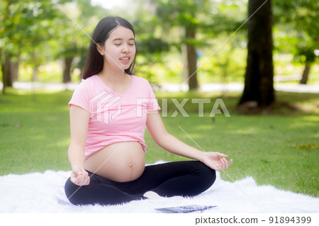 Happiness young asian woman pregnant sitting doing yoga with meditation lotus for relaxation. 91894399