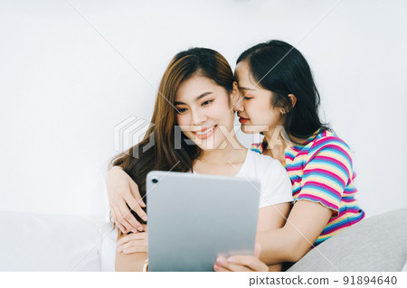 lgbtq, lgbt concept, homosexuality, portrait of two asian women posing happy together and loving each other while playing tablet on bed. lgbtq, lgbt concept, homosexuality, portrait of two asian women posing happy together and loving each other while playing tablet on bed. 91894640