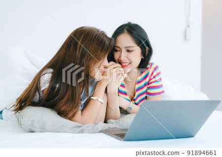 lgbtq, lgbt concept, homosexuality, portrait of two asian women posing happy together and loving each other while playing computer laptop on bed. lgbtq, lgbt concept, homosexuality, portrait of two asian women posing happy together and loving each other while playing computer laptop on bed. 91894661