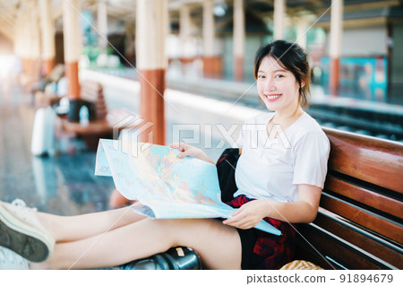 summer, relax, vacation, travel, portrait of a cute Asian girl looking at a map to plan a trip while waiting at the train station 91894679