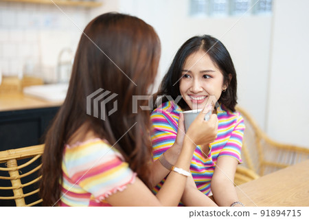 lgbtq, LGBT concept, homosexuality, portrait of two Asian women posing happy together and showing love for each other while having coffee at the dining table. 91894715