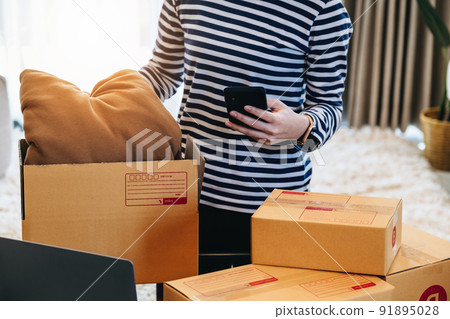 Online merchandising business idea, a beautiful girl is packing pillows in a shipping box to prepare to send items to customers according to orders received from customers 91895028