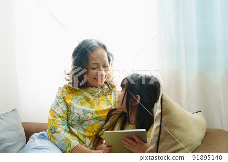 Asian portrait, Grandma and granddaughter doing recreational activities playing tablet computers on the sofa. 91895140