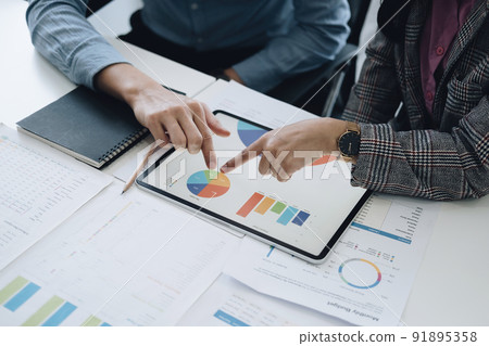 Negotiation, Analysis, Discussion, Asian young economist and marketer using tablet computer to plan investments and financial to prevent risks and losses for the company. 91895358