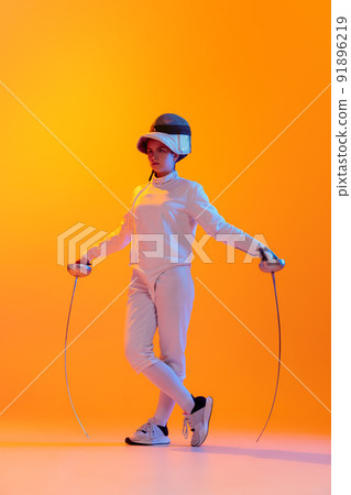 Studio shot of professional fencer in white fencing costume and mask in action, motion isolated on orange color background. Sport, youth, activity, skills, Studio shot of professional fencer in white fencing costume and mask in action, motion isolated on orange color background. Sport, youth, activity, skills, 91896219