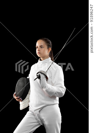 Young serious girl, beginner fencer in white fencing costume standing with rapier ans mask isolated on dark background. Sport, youth, achievements, challenges. Young serious girl, beginner fencer in white fencing costume standing with rapier ans mask isolated on dark background. Sport, youth, achievements, challenges. 91896247