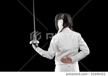 One sportsman, female fencer in white fencing costume in action, motion isolated on black background. Sport, youth, hobbies, achievements, goal. 91896422