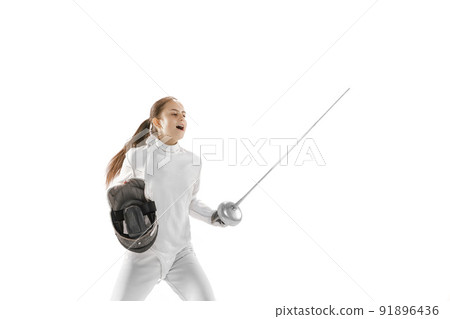 Young girl, fencer in white fencing costume posing with rapier isolated on white background. Sport, youth, hobbies, achievements, goal. 91896436