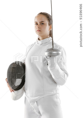 Young girl, fencer in white fencing costume posing with rapier isolated on white background. Sport, youth, hobbies, achievements, goal. 91896466