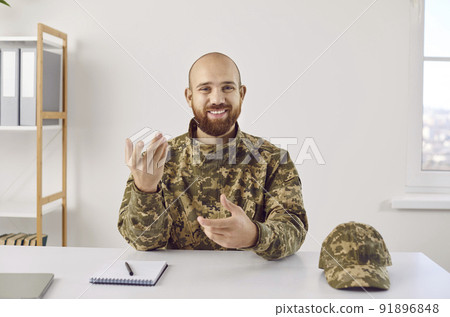 Happy soldier sitting at office desk, having conference call, speaking and smiling Happy soldier sitting at office desk, having conference call, speaking and smiling 91896848