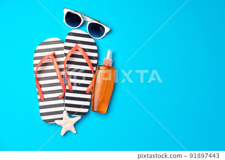 Flip-flops with sunscreen and sunglasses on blue background Flip-flops with sunscreen and sunglasses on blue background 91897443