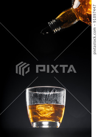 Whisky pouring into a glass on black background 91897447