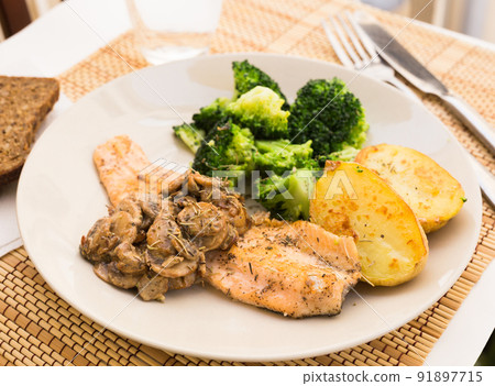 fried river trout fillet with a complex side dish of broccoli, baked potatoes and mushroom sauce 91897715