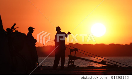 Silhouette of fishermen on the pier at sunset Silhouette of fishermen on the pier at sunset 91898123