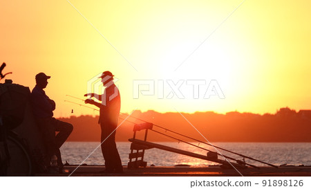 Silhouette of fishermen on the pier at sunset Silhouette of fishermen on the pier at sunset 91898126