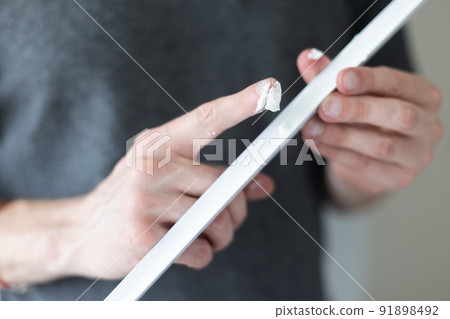 Man putting glue by finger on decorative plastic corner for the wall protection in apartment.  91898492