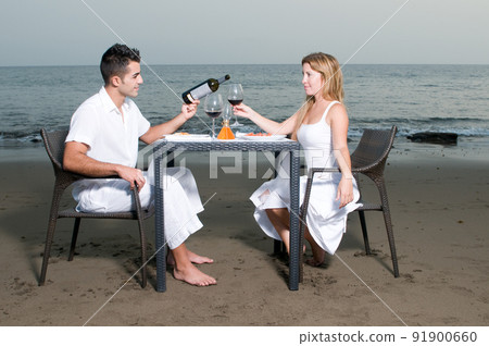 Young couple dressed in white celebrating a romantic dinner on the beach 91900660