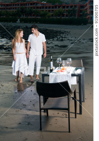 Young couple dressed in white celebrating a romantic dinner on the beach 91900705