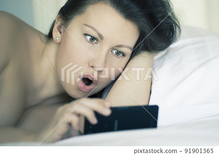 A girl lies in bed under the sheet can't fall asleep looking on mobile phone. Insomnia. Psychology. A girl lies in bed under the sheet can't fall asleep looking on mobile phone. Insomnia. Psychology. 91901365