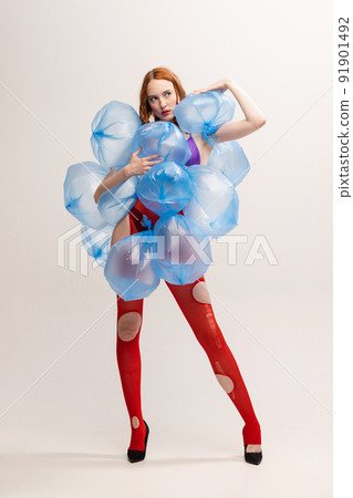 Portrait of beautiful girl with bright makeup in red torn tights posing with plastic bags with water isolated over grey background 91901492