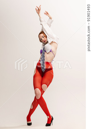 Portrait of young girl in white shirt, tie and red tights posing isolated over grey studio background. 91901493