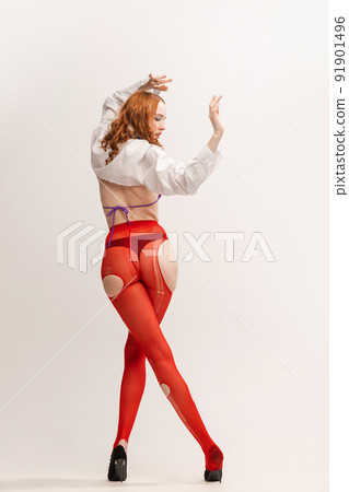 Portrait of beautiful young girl in white shirt and red tights posing isolated over grey studio background. Back view 91901496