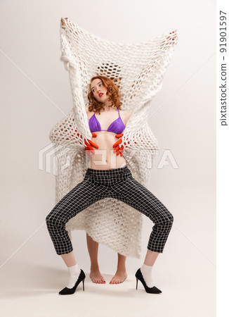 Portrait of stylish young woman dancing around knitted plaid, posing isolated over grey background 91901597