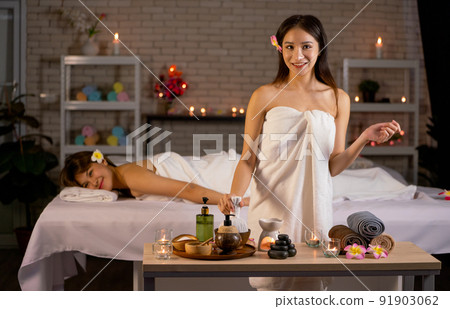 Asian beautiful woman wearing towel stand and hold herbal compress ball in front of her friend 91903062
