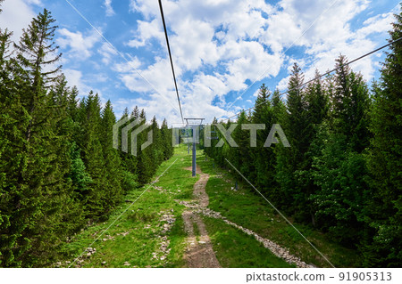 Open cable car line. Karpacz resort in Poland with lift road. Chairlift against green forest trees. Family outdoor recreation in mountains Open cable car line. Karpacz resort in Poland with lift road. Chairlift against green forest trees. Family outdoor recreation in mountains 91905313