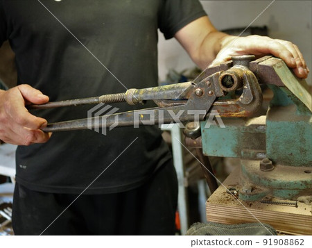 the hands of a locksmith working with a gas wrench and a vice in the workshop, a man in black clothes clamps an iron pipe in the machine and manipulates a hand tool 91908862