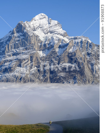 Landscape in the highlands above the clouds with man standing and looking at the mountain. Grindelwald, Switzerland. 91908873