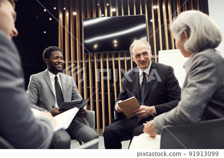 Contented multi-ethnic business people in formalwear sitting in circle in meeting room and discussing important issues at group brainstorming session Contented multi-ethnic business people in formalwear sitting in circle in meeting room and discussing important issues at group brainstorming session 91913099