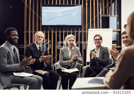 Small group of multi-ethnic business people in formal outfits sitting against business coach and applauding her after course session Small group of multi-ethnic business people in formal outfits sitting against business coach and applauding her after course session 91913105