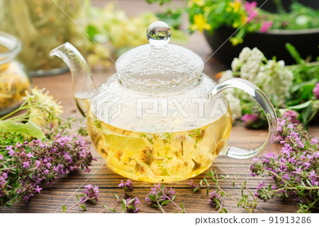 Glass tea kettle of healthy herbal tea, thyme, linden blossom, St Johns wort, yarrow, chamomile, calendula medicinal herbs on wooden table. Alternative herbal medicine. 91913286