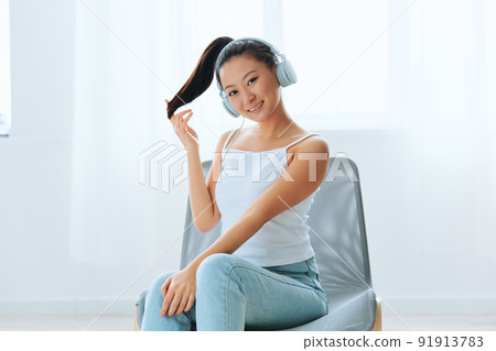 Smiling cheerful tanned lovely young Asian woman in headphones touches hair looks at camera at home interior living room. Sound Studio Stream, Social media concept. Cool offer Banner Wide angle 91913783