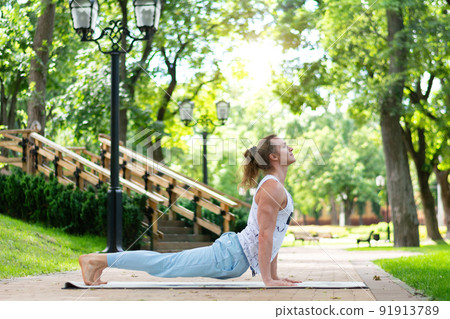 Young man practice yoga in the park. Yoga asanas in city park, sunny day. Concept of meditation, wellbeing and healthy lifestyle Young man practice yoga in the park. Yoga asanas in city park, sunny day. Concept of meditation, wellbeing and healthy lifestyle 91913789