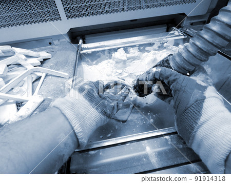A man working with a working vacuum cleaner to clean the white powder of polyamide from a model printed on a 3D printer inside a 3D printer. Cleaning objects printed on an industrial powder 3D printer 91914318