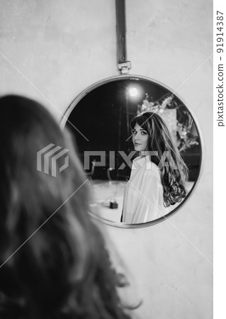a woman in a white shirt looks at reflection in a round mirror. black and white  91914387