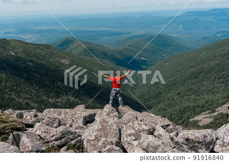 Hiker man on the top of the mountain enjoys the aerial view, raising his hands above the clouds. Mount Pidan 91916840