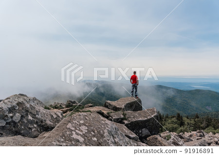 Hiker man on the top of the mountain enjoys the aerial view, raising his hands above the clouds. Mount Pidan 91916891