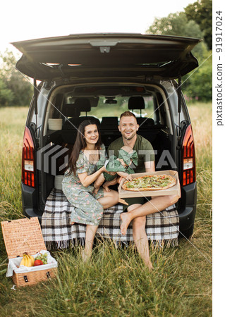 Happy young parents with dog and little daughter unpacking tasty pizza sitting on car trunk outdoors 91917024