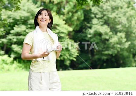 A woman using a fan in the shade of a tree A woman using a fan in the shade of a tree 91923911